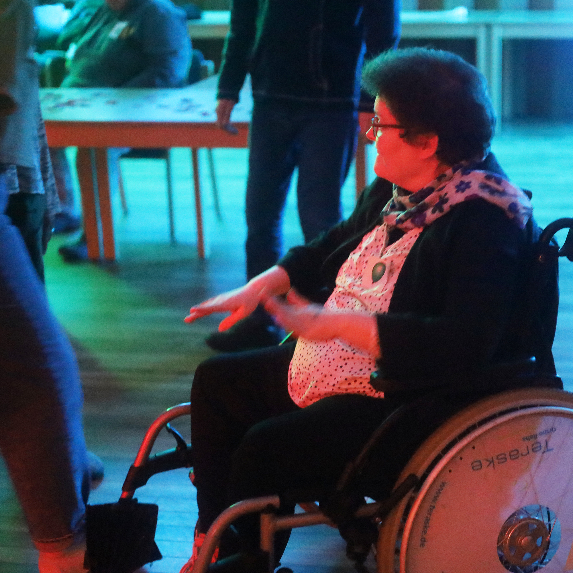 Eine Frau im Rollstuhl ist auf einer Party. Sie hebt die Hände zur Musik.